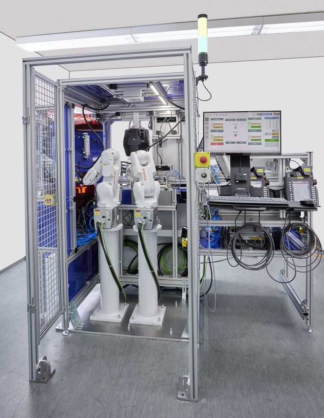 Automatisierte KUKA-Roboteranlage mit zwei Roboterarmen, Schutzgehäuse und Steuerungsmonitor in einer modernen Produktionsumgebung.