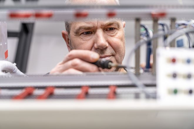 Mitarbeiter prüft konzentriert elektrische Anschlüsse und Komponenten an einem technischen Prüfstand.